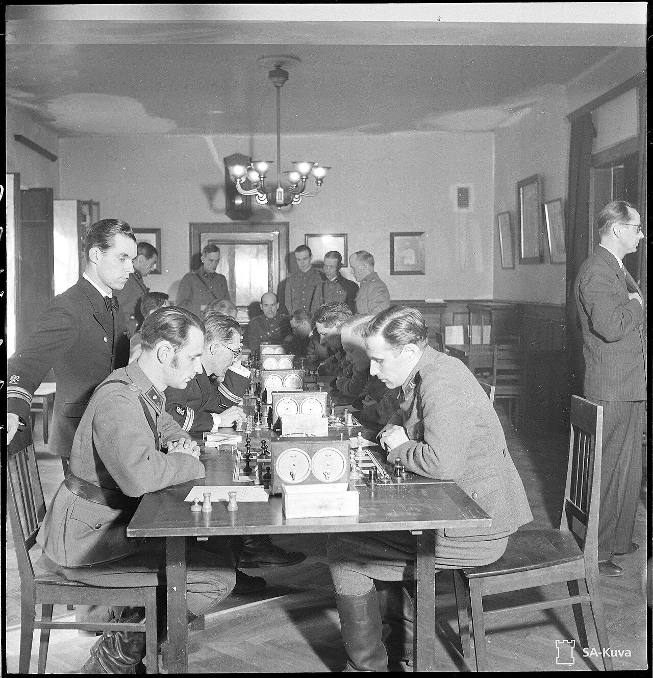 A chess club evening in Helsinki, 1941: players concentrating over boards and clocks while others watch.