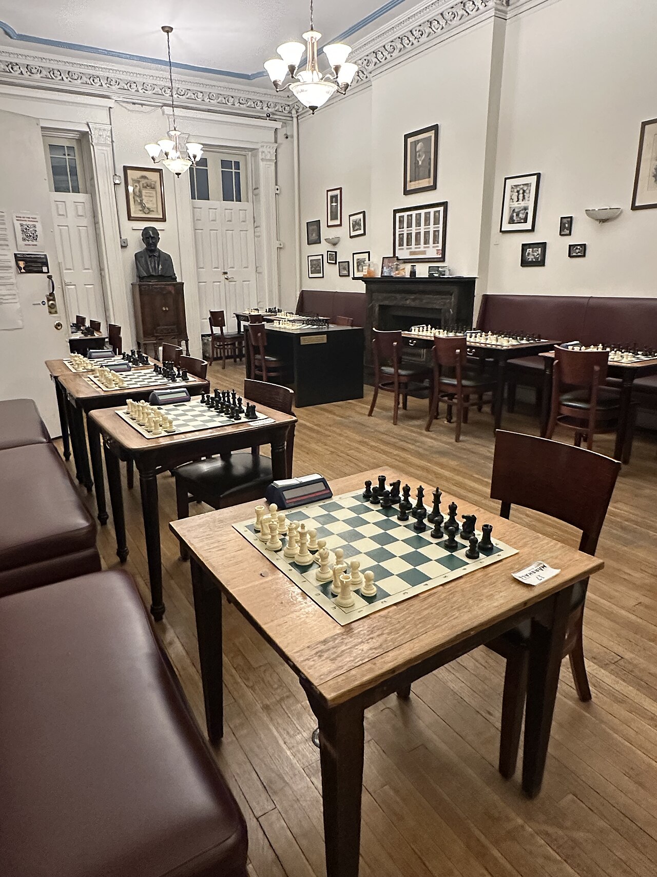 The playing room of a traditional chess club: rows of wooden tables, each set with a board, pieces and a clock, waiting for the evening’s players.